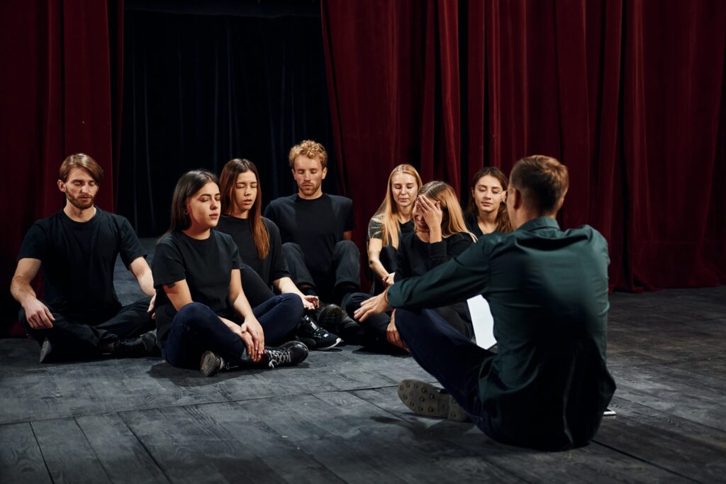 Sitting on the floor. Group of actors in dark colored clothes on rehearsal in the theater