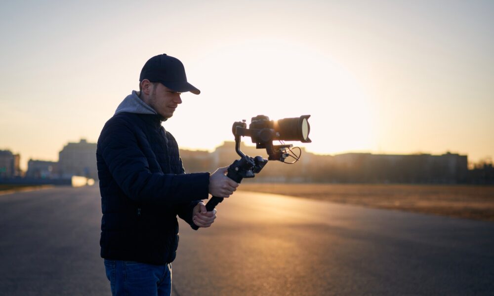 Young man filming with camera and gimbal. Filmmaker standing against city at sunrise. Prague, Czech