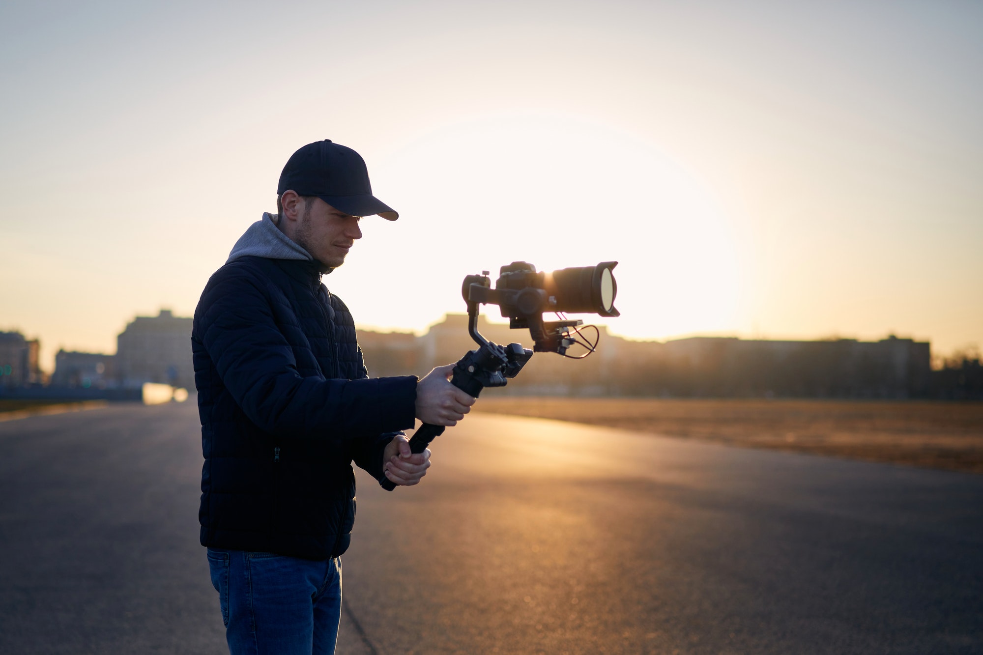 Young man filming with camera and gimbal. Filmmaker standing against city at sunrise. Prague, Czech